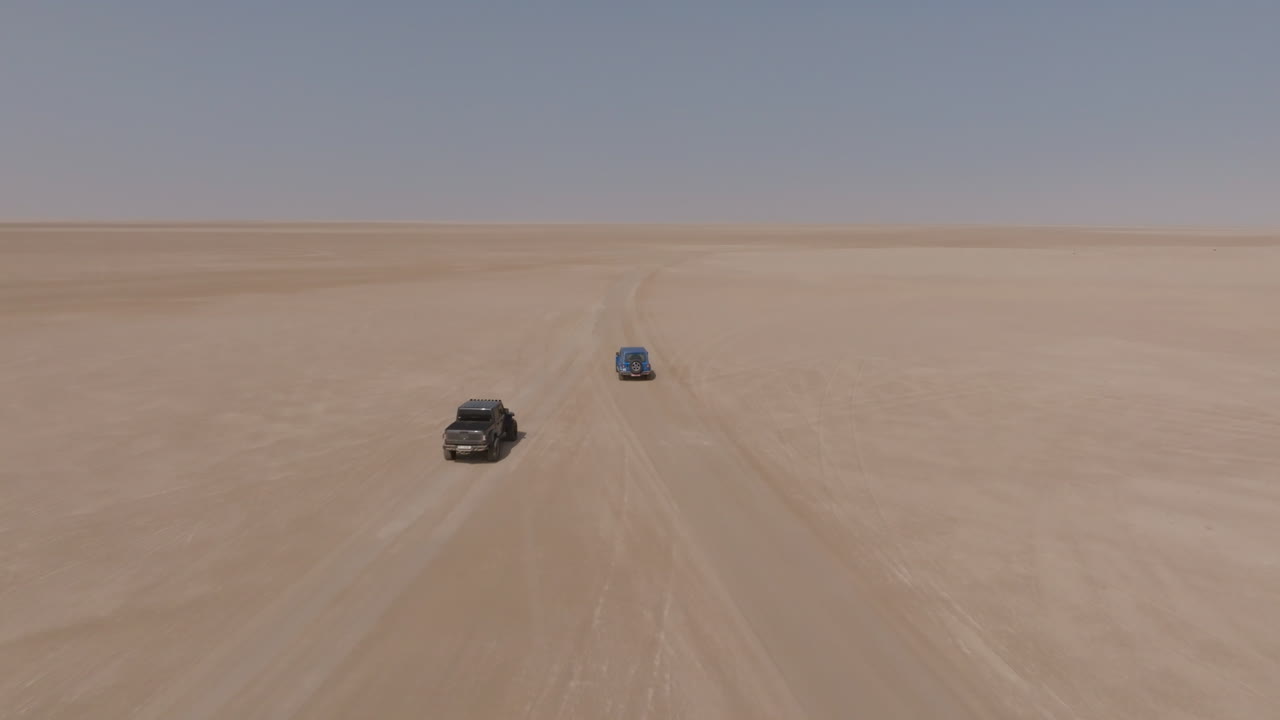 Two SUVs driving through vast desert in Bar al Hikman, Oman, aerial daytime shot