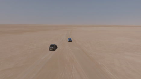 two suvs driving through vast desert in bar al hikman, oman, aerial daytime shot