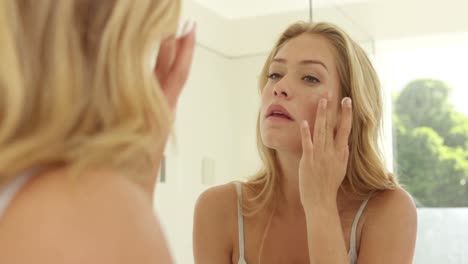 young woman applying cream on her face