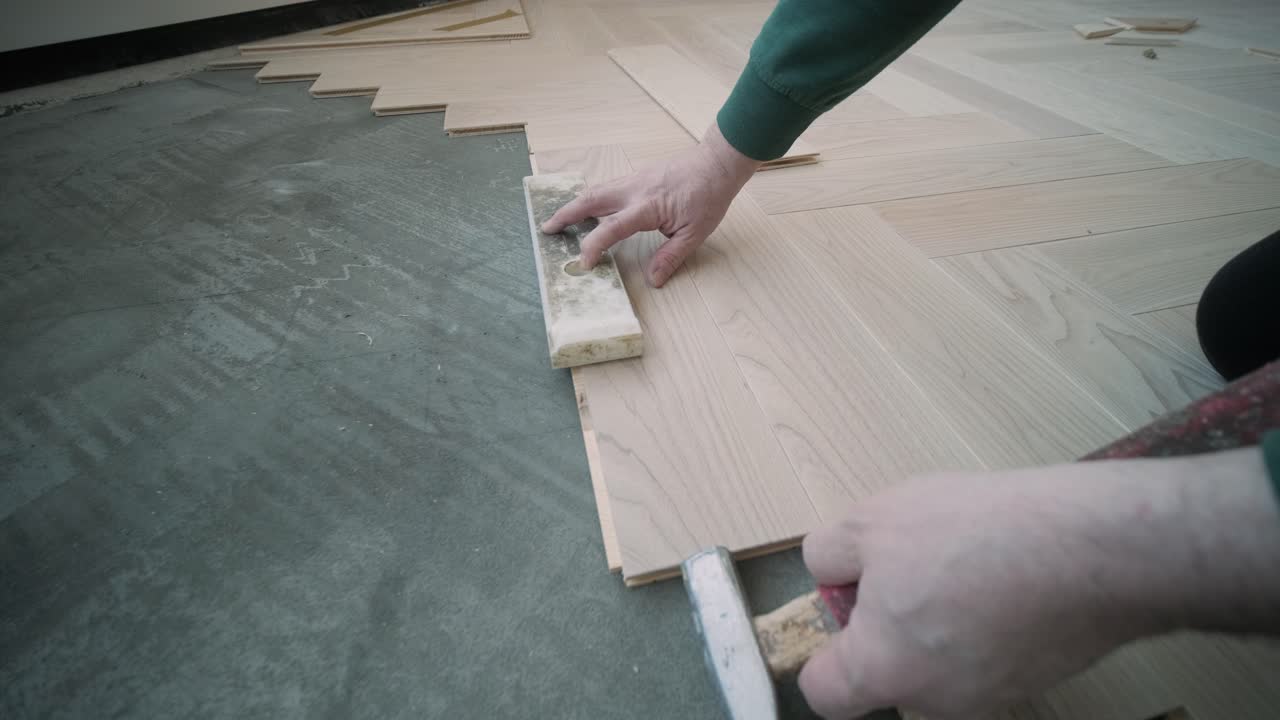 Worker installing wooden flooring with hammer and tapping block
