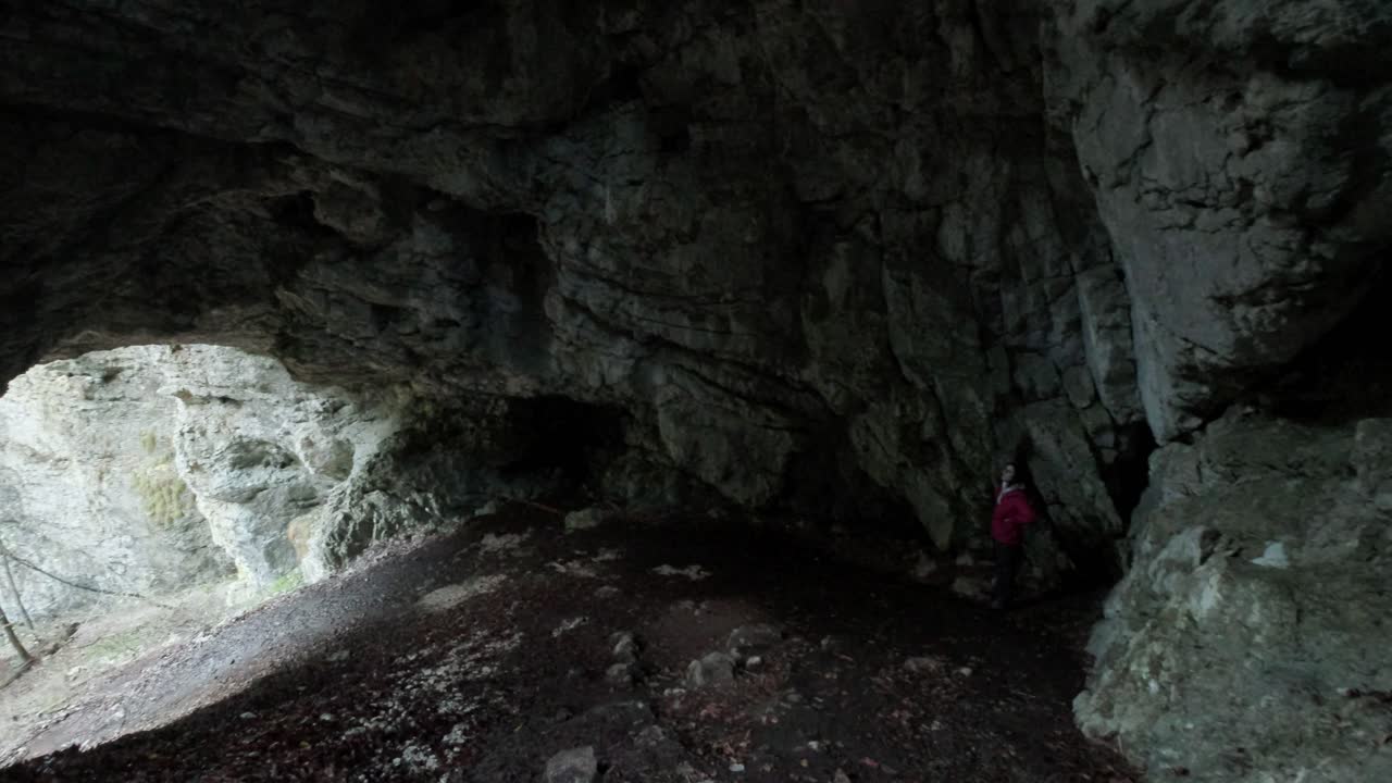 Lady standing in Pokljuka Cave with the camera panning from right to left to show the cave entrance. Pokljuka Gorge in Slovenia Triglav National Park