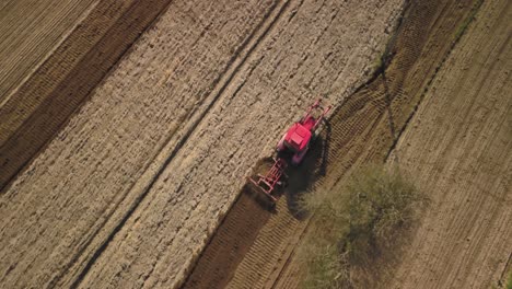 aerial top down red tractor plowing land in farm preparing for seeding food production