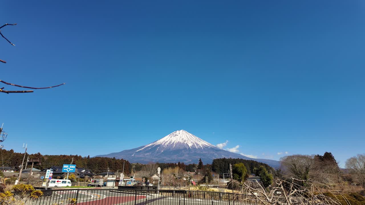 冬日枯枝後方漸現富士山白雪皚皚的山峰，背景是寧靜日本小鎮的深藍色天空，捕捉到清澈明朗的一天。