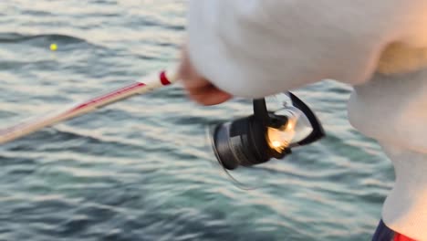 close up of man reeling in a fishing rod by the sea