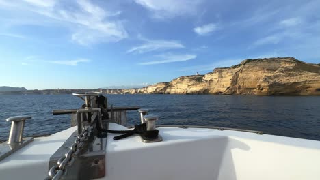 Point-of-view-of-sailboat-bow-navigating-toward-Corsica-island-cliffs-and-Capo-Pertusato-lighthouse-in-France,-50fps-1