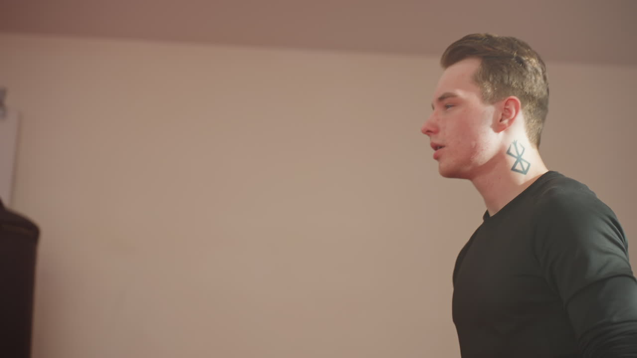 Boxer standing in gym adjusting hair after training session, wearing black shirt, visible neck tattoo, focused expression, moment of rest and self-reflection after workout, showing strength, discipline