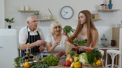 Senior-couple-in-kitchen-receiving-vegetables-from-granddaughter.-Healthy-raw-food-nutrition