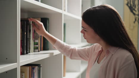 girl customer chooses book on store shelf. brunette woman seeks interesting literature for leisure in bookstore. constant reader finds new historical novel