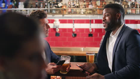 dos hombres de negocios chequeando teléfonos móviles mientras se reúnen para tomar una copa en un bar