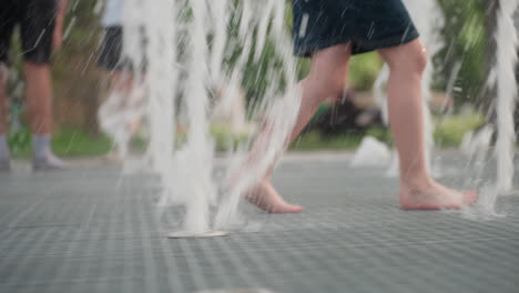 young girl running barefoot across splash fountain, leg view showing motion and water streams on grid surface, summer park play, joyful energy, wet droplets scattering, casual childhood activity