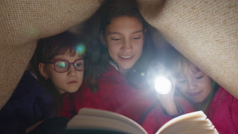 children girl kids under blanket reading interesting fairytale story book using flashlight at home