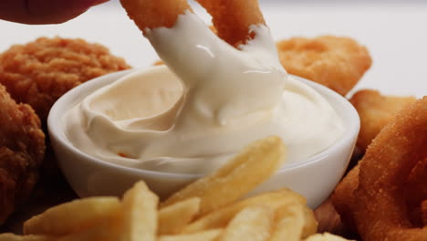 dipping onion rings and chicken nuggets in mayo sauce with french fries