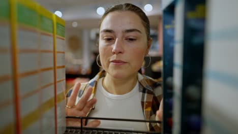 Close-up-a-confident-brunette-girl-in-a-checkered-shirt-examines-the-goods-on-the-counter-and-chooses-the-product-she-needs-in-the-supermarket