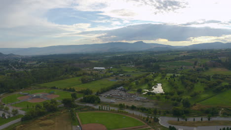 vista aérea de campos, bodegas, un diamante de béisbol, lagos y montañas fuera de kelowna, en un día de verano