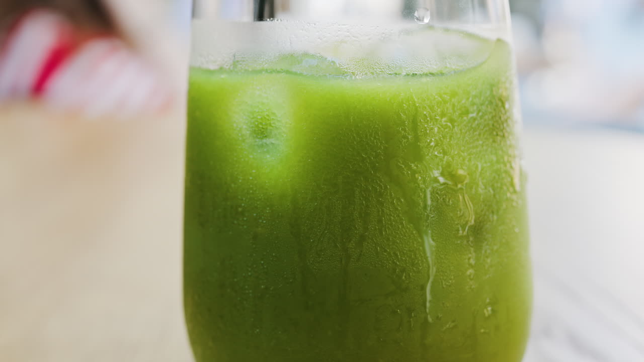 Close up of a glass of an iced orange juice matcha on a table at a cafe
