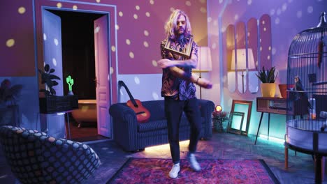 young stylish caucasian man with long hair holding empty frame and dancing energetically in a retro party at home