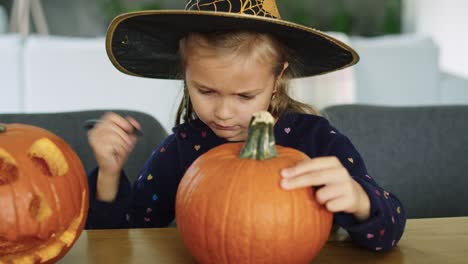 girl in halloween costume drawing on pumpkin