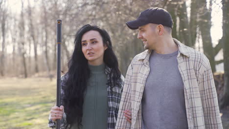 caucasian couple hugging while holding a wheelbarrow and a rake in the countryside