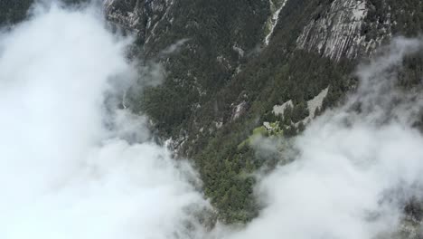 drone-aerial-reveal-flying-through-a-big-cloud-of-a-waterfall-and-a-small-village-on-the-side-of-a-mountain-in-northern-italy