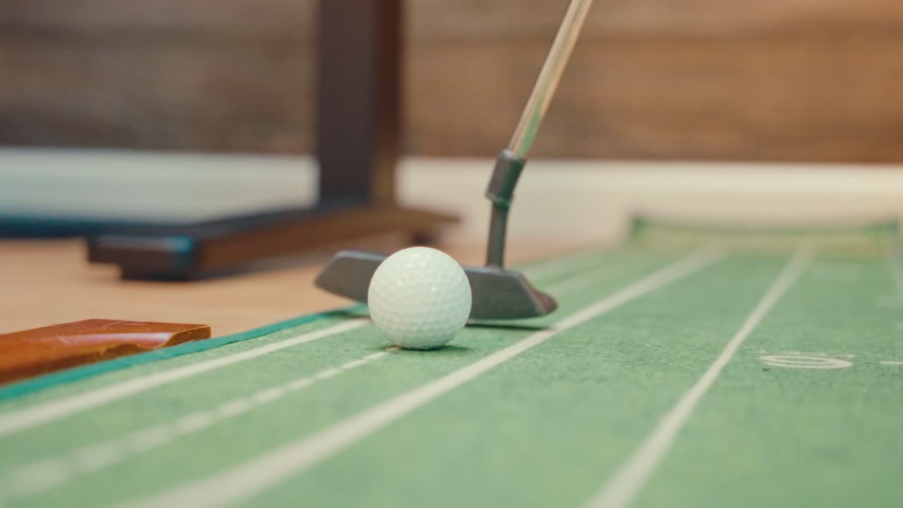 Zpomalený záběr zblízka putteru odpalujícího golfový míček na vnitřní tréninkové podložce. Golfová tréninková videa, cvičení patování, praxe a reklamy na produkty