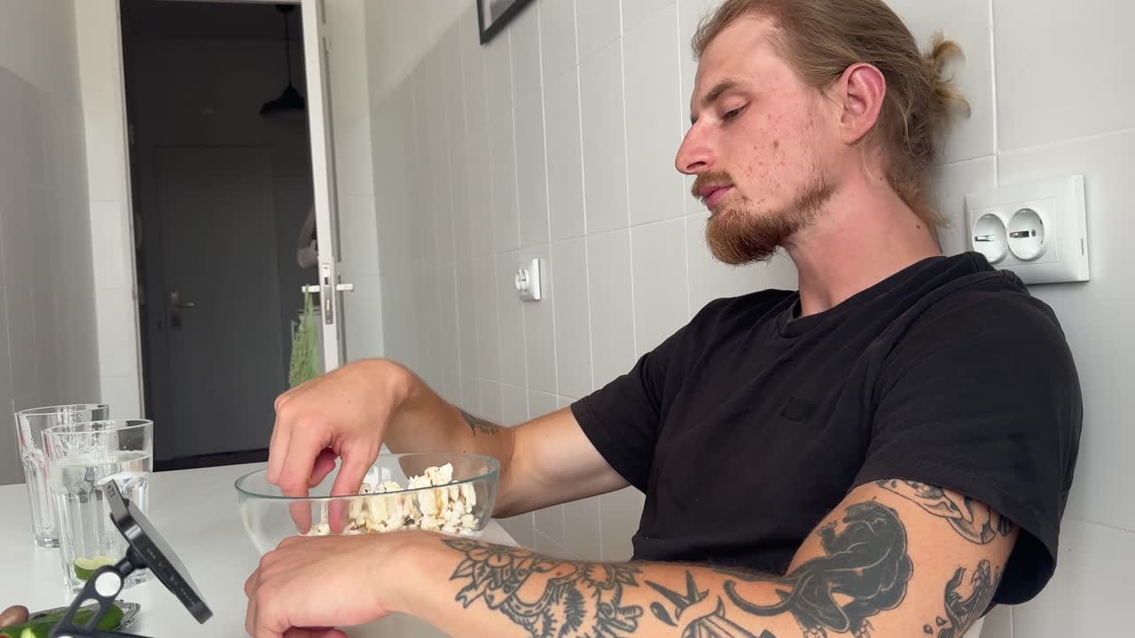 Uomo casual con barba e tatuaggi che mangia popcorn.
