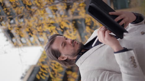 Bearded-businessman-standing-at-the-street-and-tapping-with-stylus-on-gadget-computer