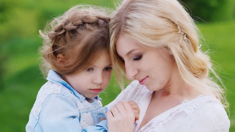 Madre-Bellamente-Vestida-Con-Su-Hija-Abrazar-Suavemente-Contra-El-Fondo-De-Follaje-Verde