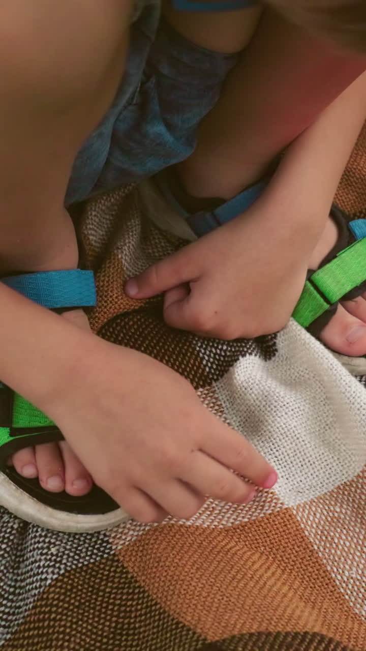 primer plano de un niño en cuclillas sobre una manta a cuadros con una mano tocándola y la otra mano descansando en su pierna, usando una sandalia verde