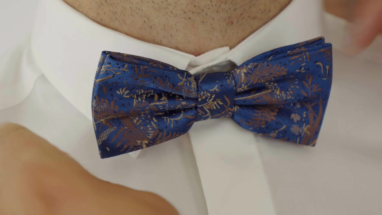 I preparativi dello sposo per il matrimonio, con il testimone che gli sistema il papillon blu al collo.