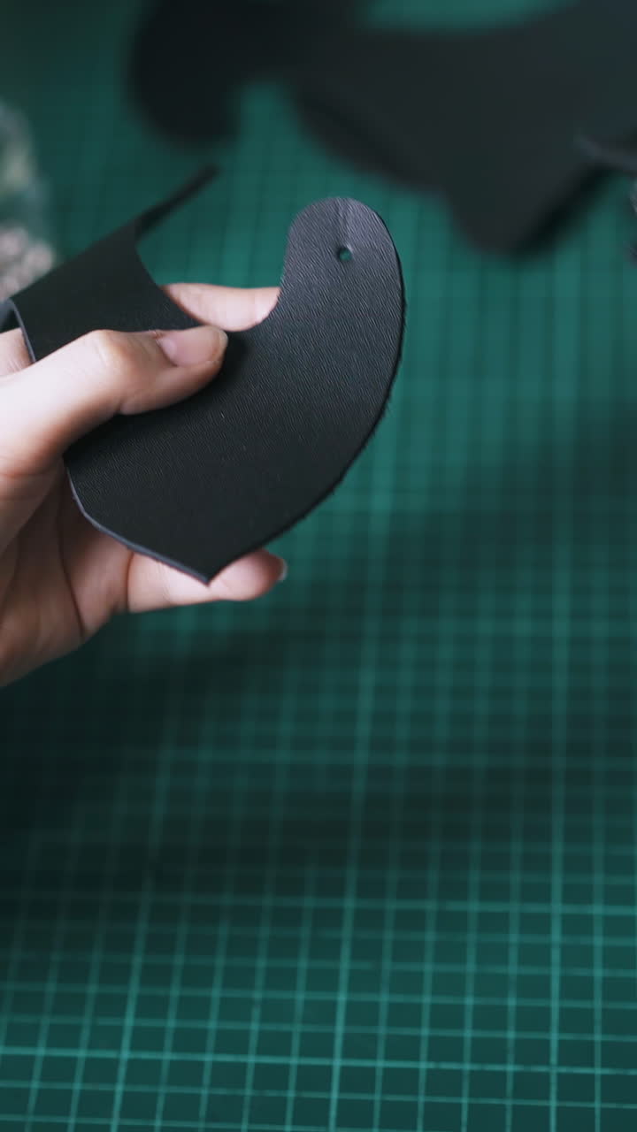 CU: Experienced tailor makes holes in black leather cat mask ear with punch pliers in workshop extreme close view