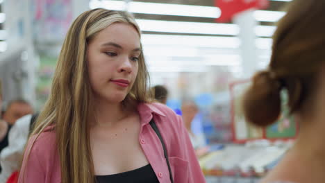 white lady in pink dress inside a well-lit mall waiting in line to pay for items, takes a deep breath as she moves forward, other shoppers and a working man are visible in the blurred background