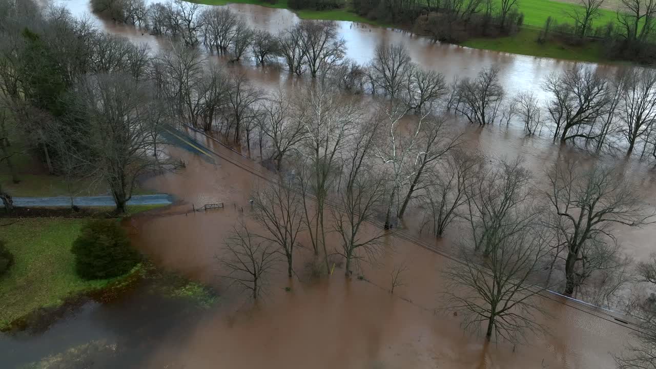 Aerial top down shot of flooding river with bare trees in winter after large rain in American suburb