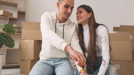 zoom out shot of a young couple in a new house sitting on the carpet assembling a furniture