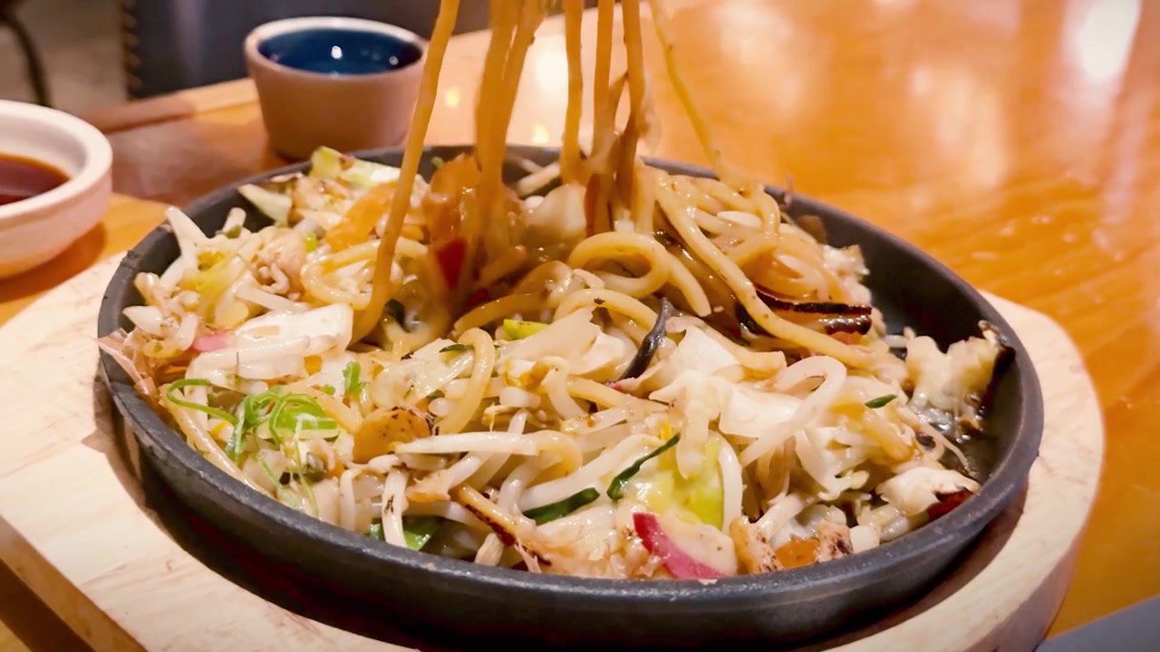 Des baguettes soulèvent des nouilles yakisoba japonaises fumantes avec des crevettes et des flocons de bonite d'une poêle