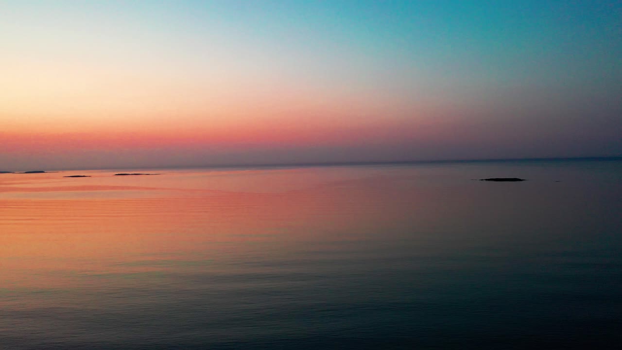 드론이 평온한 바다 위로 내려가는 아름다운 해가 뜨고 지평선에 작은 섬들이 있습니다.