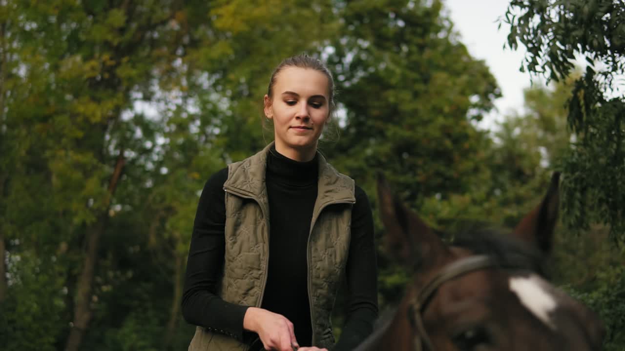 Close Up view of young beautiful woman stroking brown horse while sitting in the saddle and putting her head on the horse's head