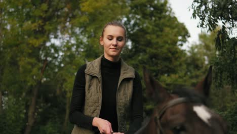 Vista-De-Cerca-De-Una-Joven-Hermosa-Mujer-Acariciando-Un-Caballo-Marrón-Mientras-Estaba-Sentada-En-La-Silla-Y-Poniendo-Su-Cabeza-Sobre-La-Cabeza-Del-Caballo