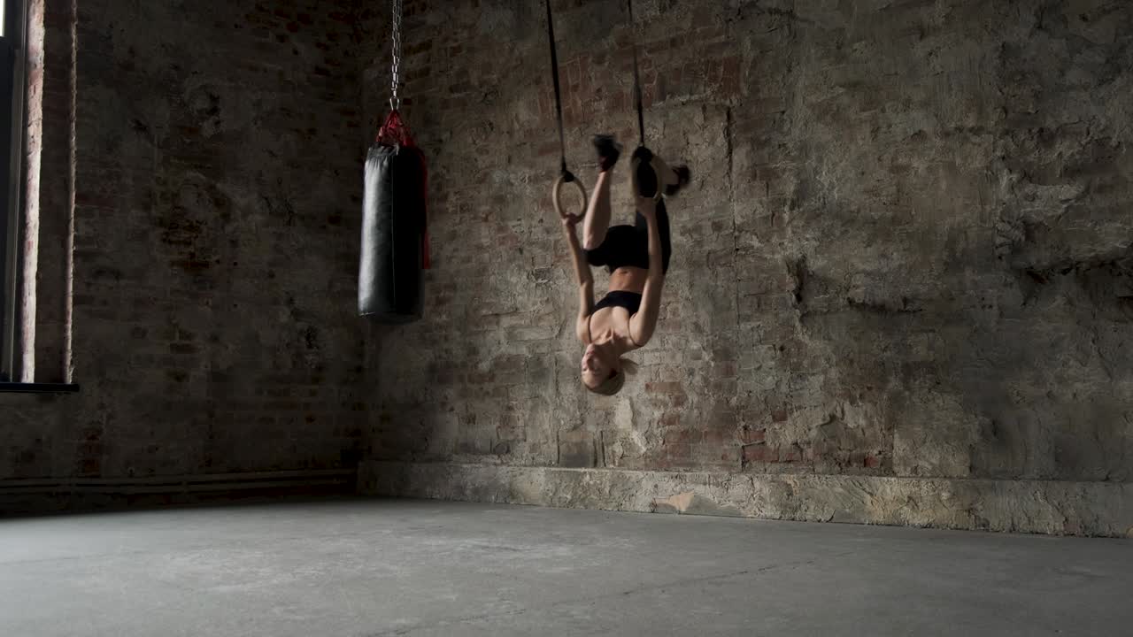 chica deportiva haciendo saltos en anillos deportivos. joven mujer en forma haciendo estiramientos en anillos de gimnasia. joven atleta femenina musculosa haciendo ejercicios con anillos en el gimnasio. joven chica en forma haciendo pull-ups en anillos gimnásticos