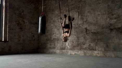 sporty girl doing flips on sports rings. young fit woman doing stretching on gymnastic rings. muscular young female athlete exercising with rings at gym. young fit woman doing pull-ups on gymnastic rings