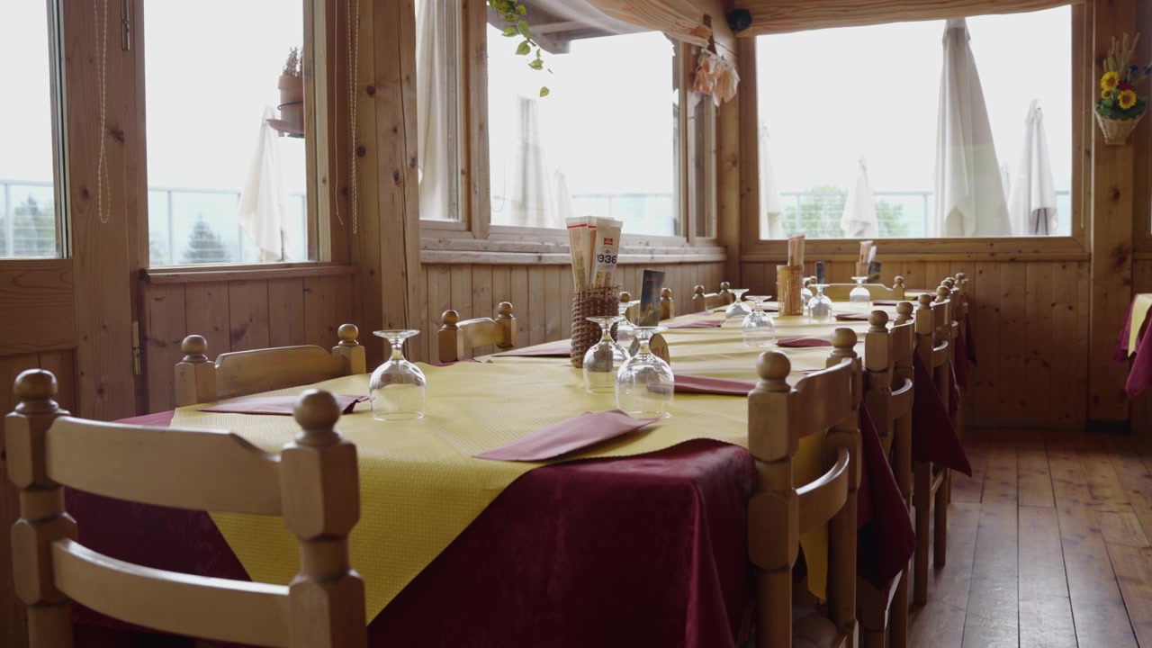 Rustic wooden interior of a cozy alpine lodge dining room in Italy. Set tables by large windows overlooking the mountains inside a traditional mountain chalet or retreat