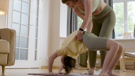 entrenador en ropa deportiva levantando a una joven para hacer la pose de la rueda de yoga