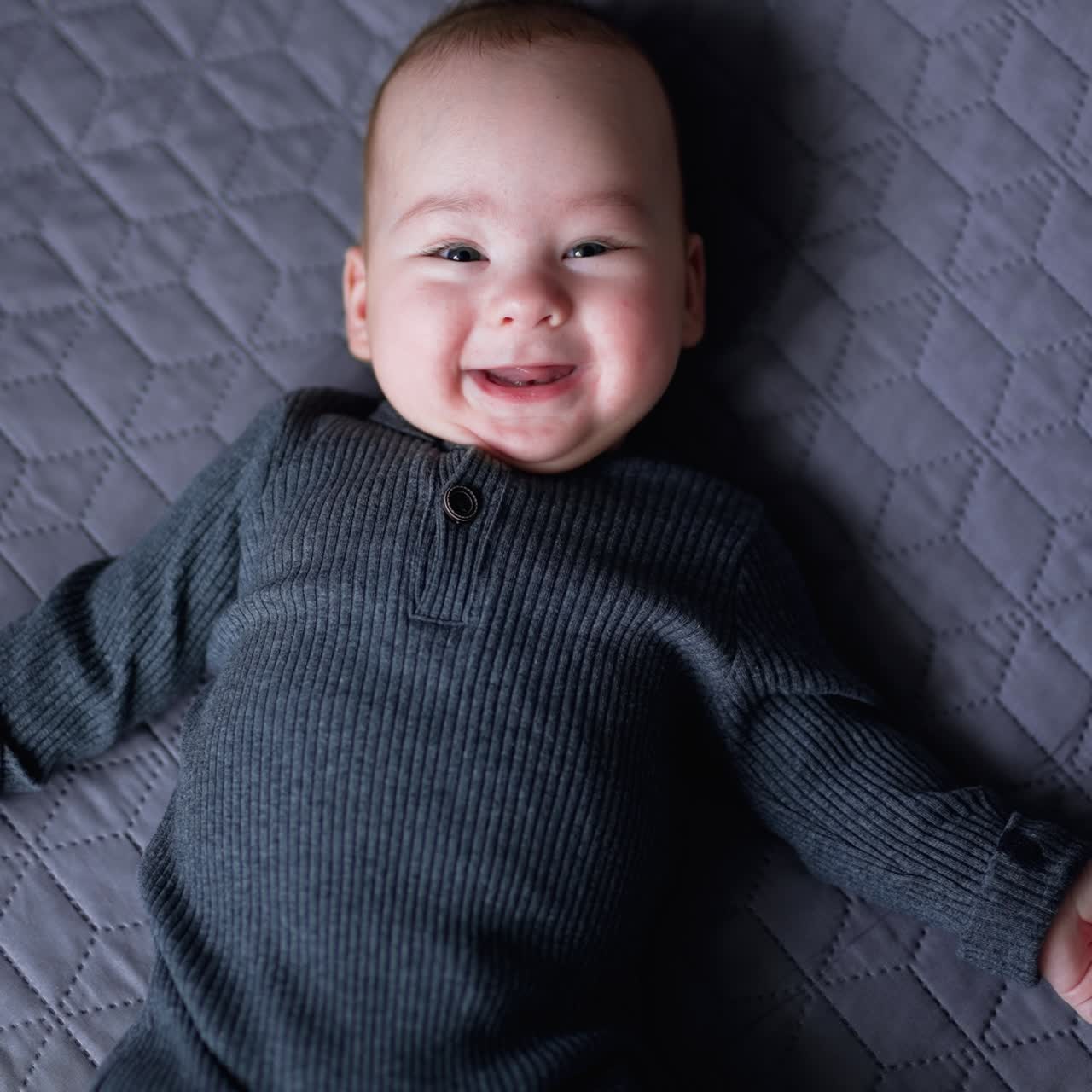 A nice little caucasian baby funnily smiling to the camera, lying at the back on bed. Portrait of a playful and energetic child close-up