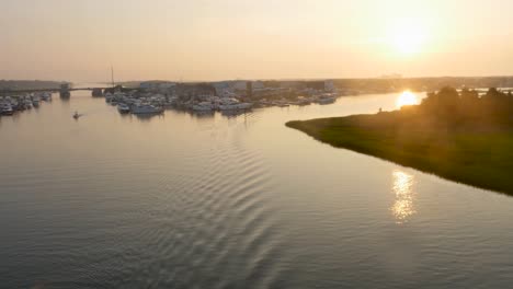 4k-view-of-small-beach-town-at-sunrise-over-the-water-way-revealing-boats-and-green-marsh-early-in-the-morning,-rotating-right-to-left