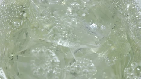 close-up show of clear ice in a glass into which a slightly green bubbly drink is poured