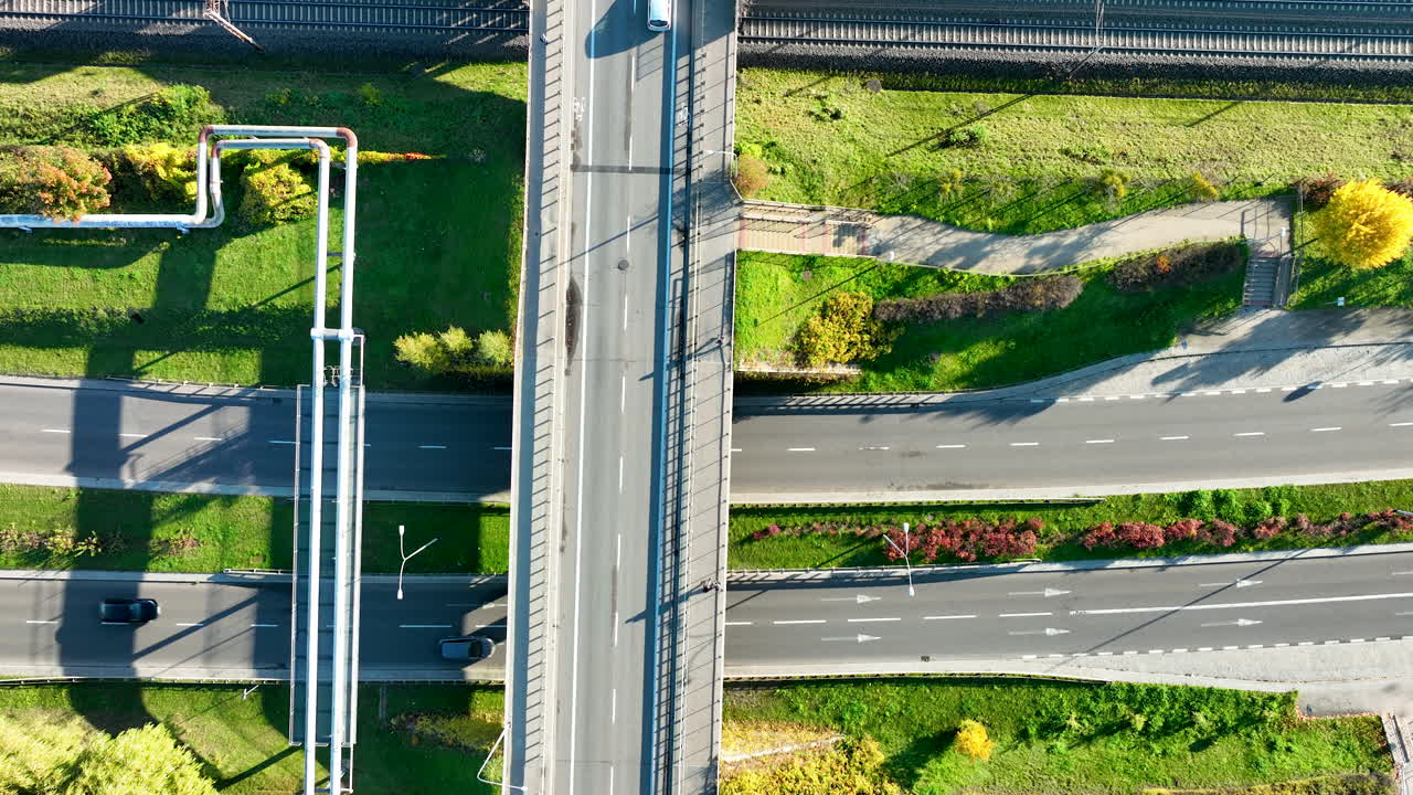 Top-down aerial drone shot of complex urban road and rail infrastructure, featuring an overpass, underpass, and ground-level roads with a pedestrian crossing
