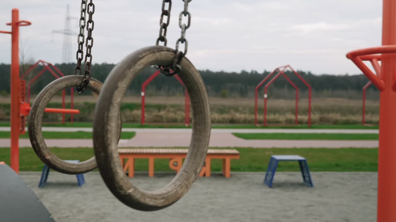 놀이터에서 흔들리는 체조 링: 스포츠 장비를 갖춘 빈 현대적인 놀이터, 코로나 바이러스 팬데 기간 동안 놀이터에 사람이 없습니다.