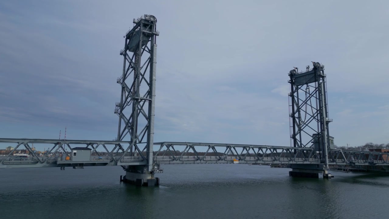 Drone captures impressive architecture of Memorial bridge with light traffic crossing over Piscataqua river in Portsmouth, New Hampshire, USA, under cloudy sky.