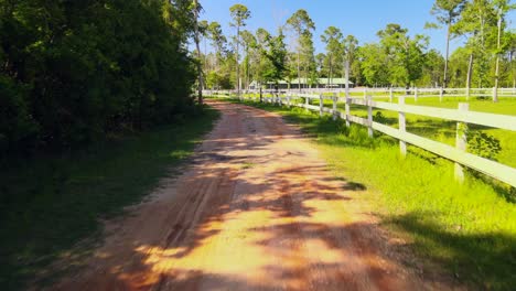 a drone flying along a path leading up to a beutiful horse ranch with white picket fences