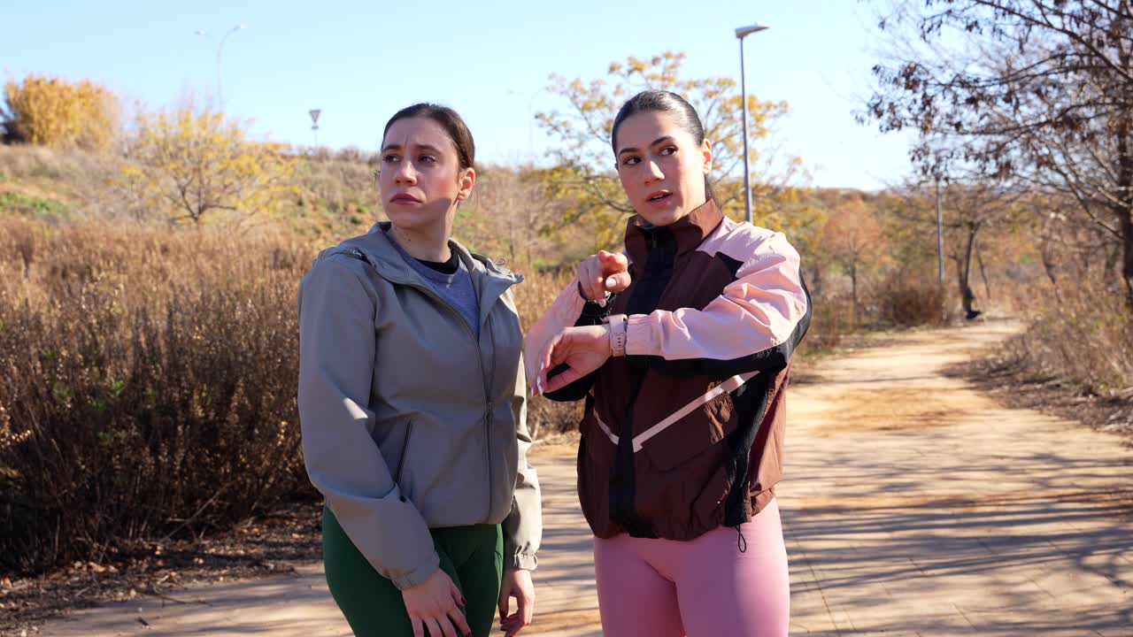 Trainer woman shows training plan pointing at her smartwatch, outdoor running session