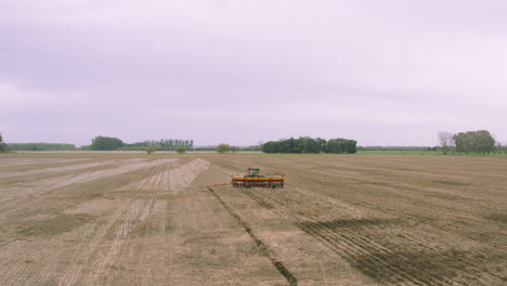 AERIAL---Harvester-tractor-cultivating-land,-agriculture-field-at-dawn,-forward